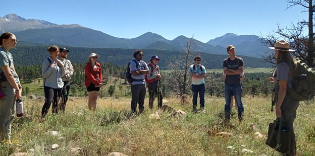 八个学生站在山脉前和一个公园管理员谈话.